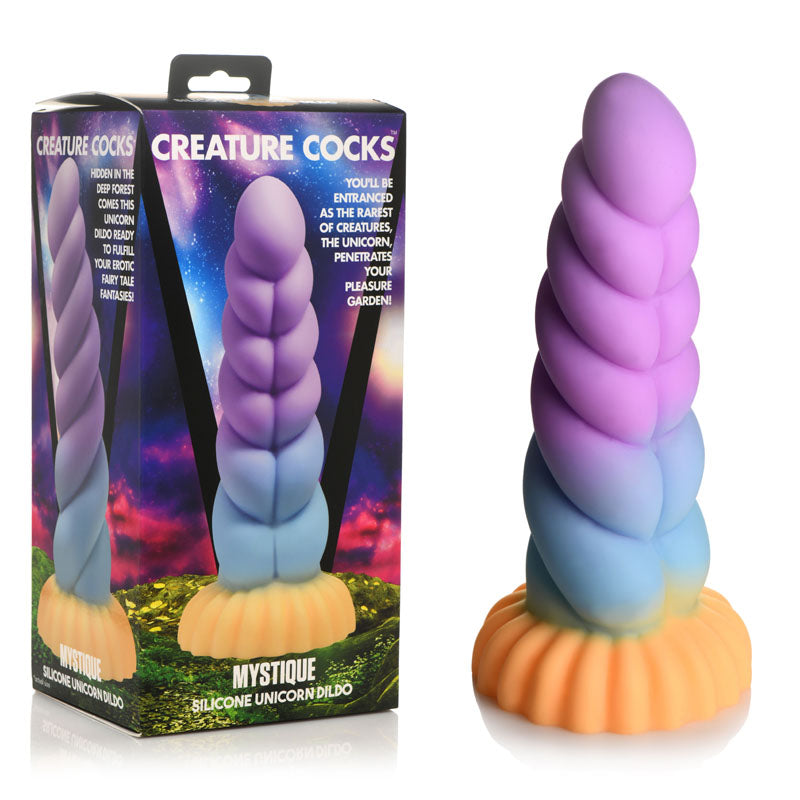 The Creature Cocks Mystique Silicone Unicorn Dildo, a 21 cm premium fantasy dildo, boasts a pastel unicorn horn design in purple, blue, and yellow with a suction cup base. It comes with an orange stand and its box features a vibrant mystical forest scene.