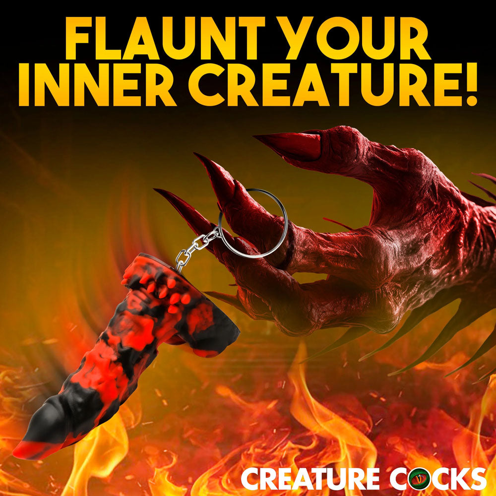 A demonic, clawed hand displays the Creature Cocks Fire Demon Keychain amid flames. Flaunt Your Inner Creature! appears above, while CREATURE COCKS decorates the bottom, inviting fantasy roleplay in a mystical setting.