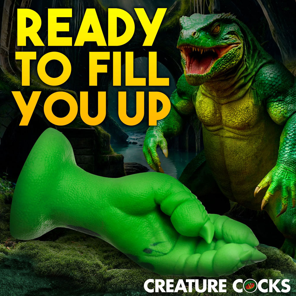 A green Creature Cocks Raptor Claw Fisting Silicone Dildo is showcased in the foreground. The background depicts a humanoid lizard in a shadowy jungle, with bold yellow text stating READY TO FILL YOU UP and the brand name CREATURE COCKS at the bottom.