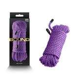 The image displays the Bound Rope - Purple Bondage Rope, a non-chafing polyester fiber rope, neatly coiled near its black packaging with a display cut-out and Bound in bold gold letters. At 7.6 meters long, it’s ideal for various uses.