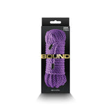 Close-up of a black box with coiled, braided purple rope made from non-chaffing polyester fiber, labeled 25 ft. (7.62m) and Bound in gold text, displaying the brand ns novelties at the bottom and featuring a hanging tab at the top. Product Name: Bound Rope - Purple Bondage Rope - 7.6 metre length.