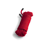 The Bound Rope - Red Bondage Rope, measuring 7.6 meters, is coiled into a neat cylindrical shape with black plastic end caps, displayed on a white background. Its tightly wound polyester fibers highlight the rich red color and texture, while subtle shadows to the left add depth to the image.