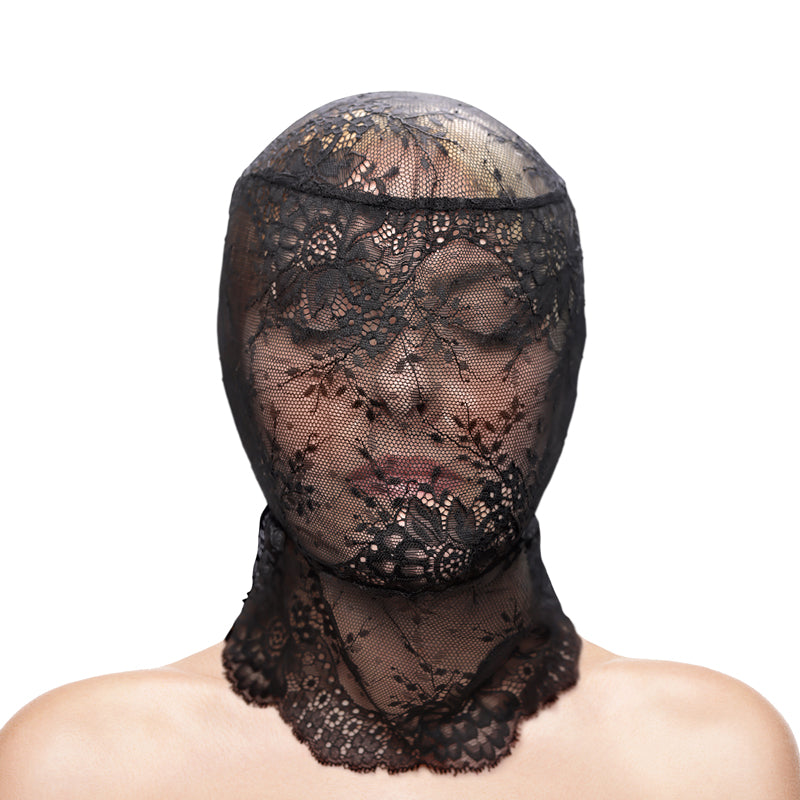 A person wears the Fetish & Fashion - Lace Hood, featuring intricate floral patterns. The stretch lace softly covers their closed eyes, with skin subtly visible beneath. A plain white background elegantly emphasizes the black hoods delicate details.