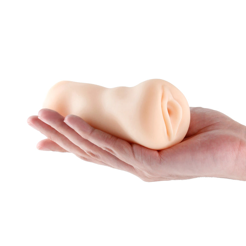 A hand grips the Barely Legal - Christine - Flesh Vagina Stroker, a light flesh-toned silicone object with a smooth, cylindrical shape and subtly curved design, while the plain white background accentuates its textured shaft and highlights its allure.
