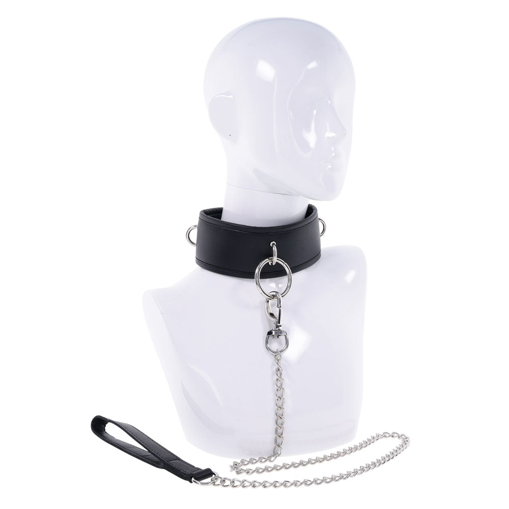 The EDGE Collar & Leash is exhibited on a white mannequin bust, showcasing a padded black faux leather design with metal rings and a central loop connecting to a detachable silver chain leash. The leash has a black loop handle, and the mannequin lacks facial features.
