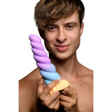 A shirtless person with short, wavy hair holds the Creature Cocks Mystique Silicone Unicorn Dildo, a colorful pastel purple, blue, and orange fantasy dildo. Resembling a soft serve ice cream cone and made of premium silicone, they smile slightly at the camera against a plain white background.