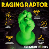 Presenting the Creature Cocks Raptor Claw Fisting Silicone Dildo—a 21.8 cm green, dinosaur claw-shaped toy made from premium silicone. Ideal for fantasy roleplay with its phthalate-free design, it includes harness compatibility and a strong suction base, set against a dark cavernous backdrop.