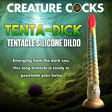 A multi-colored, 32 cm Creature Cocks Tenta-Dick silicone tentacle dildo with a strong suction-cup base stands upright in an underwater setting with seaweed, rocks, and a sea urchin illuminated by sunlight. Text reads Creature Cocks on this phthalate-free fantasy product.